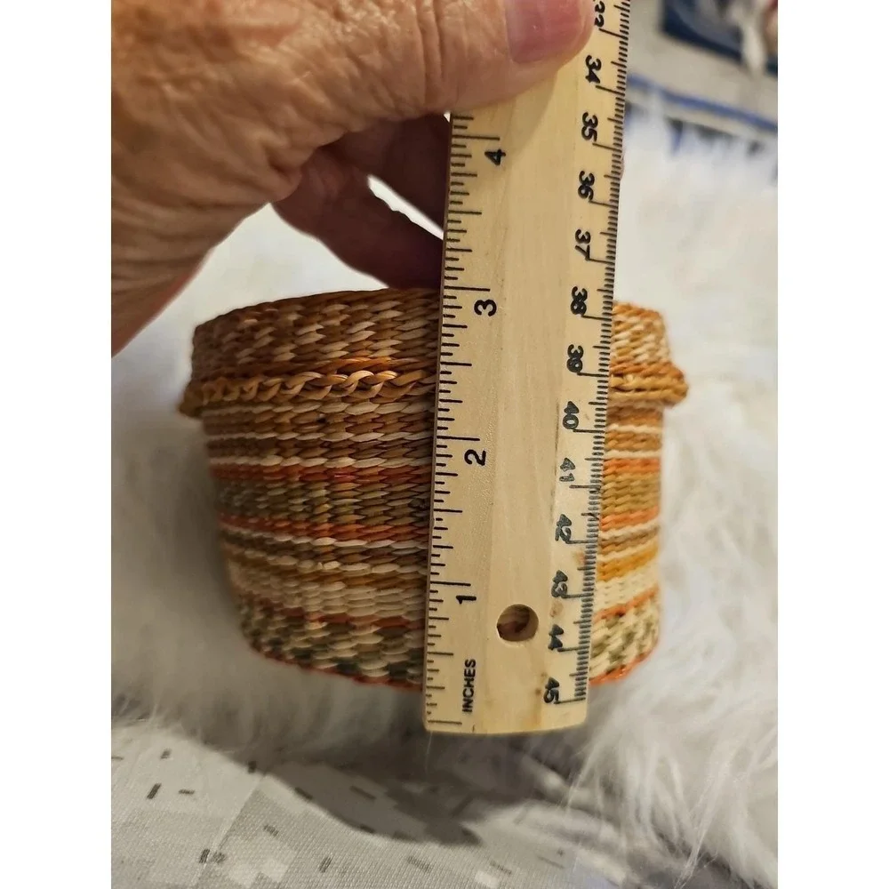 The image displays a‎ small, round, hand-woven basket with a lid, typically made